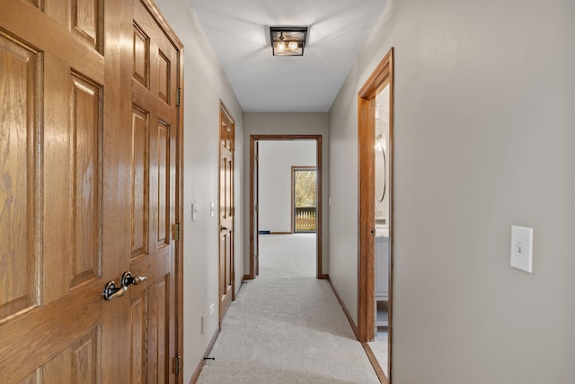 hallway with baseboards and light colored carpet