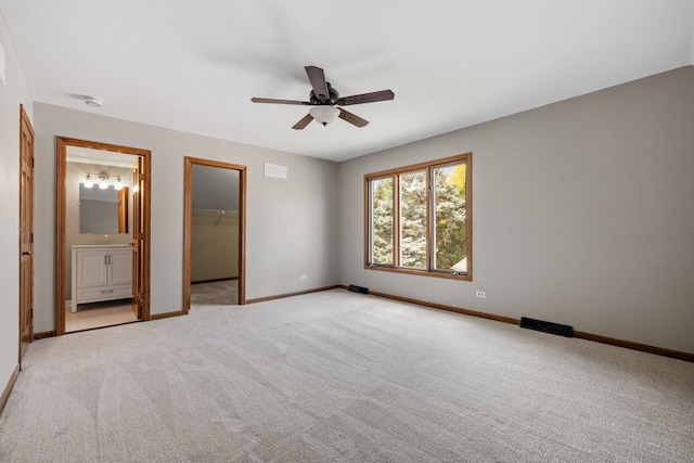 unfurnished bedroom featuring visible vents, baseboards, light colored carpet, a spacious closet, and a ceiling fan