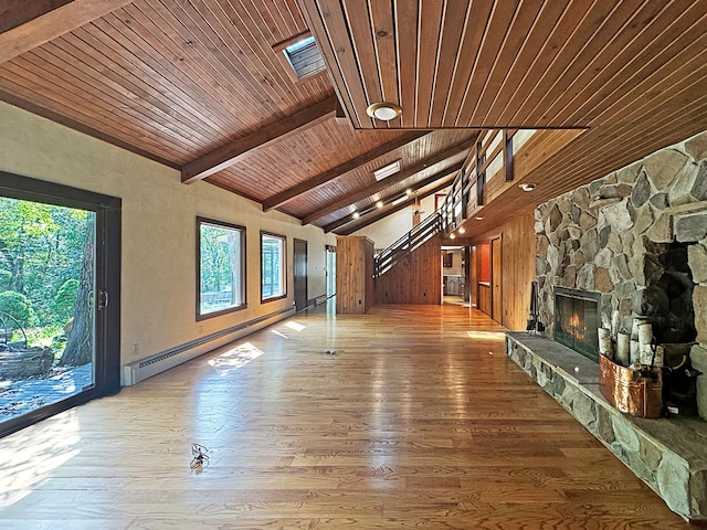 unfurnished living room featuring vaulted ceiling with beams, a stone fireplace, baseboard heating, and wood finished floors