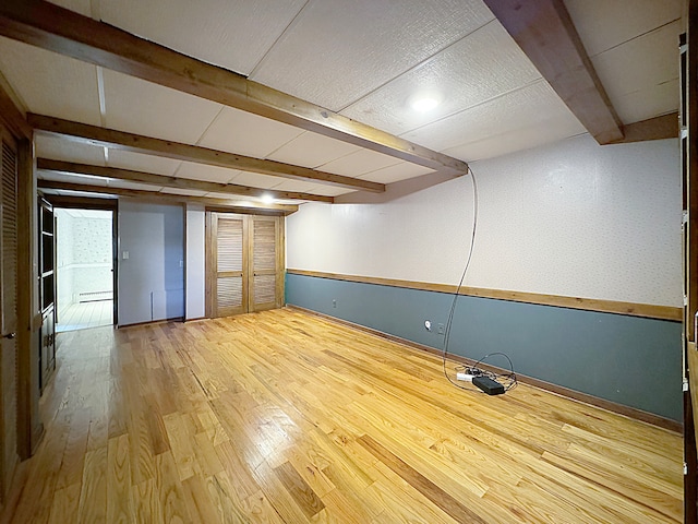 empty room with wainscoting, beamed ceiling, baseboard heating, and wood finished floors