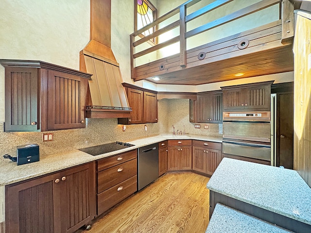 kitchen with tasteful backsplash, appliances with stainless steel finishes, light wood-style floors, a sink, and light stone countertops