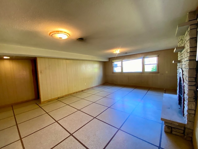 basement with a textured ceiling, wood walls, light tile patterned floors, and a stone fireplace