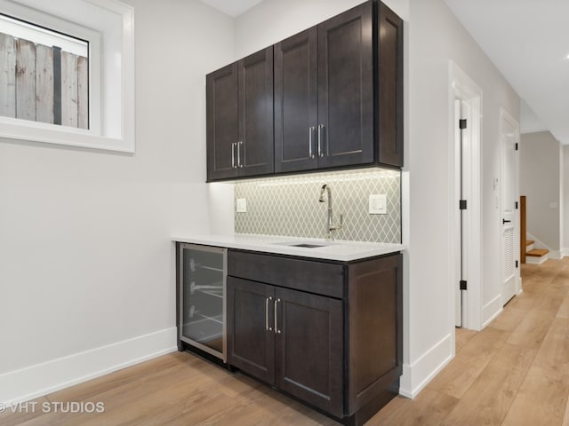 bar with light hardwood / wood-style flooring, wine cooler, sink, and dark brown cabinetry