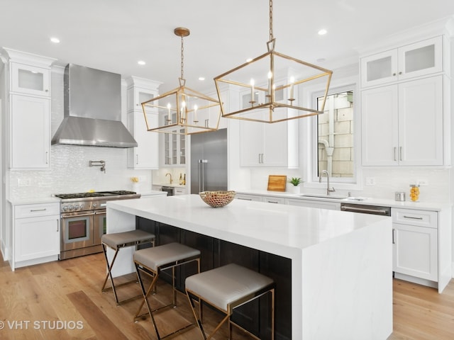 kitchen with pendant lighting, high quality appliances, light hardwood / wood-style floors, a chandelier, and wall chimney range hood