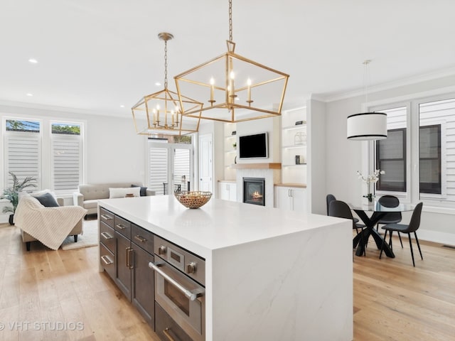 kitchen with a notable chandelier, crown molding, light hardwood / wood-style flooring, decorative light fixtures, and a kitchen island