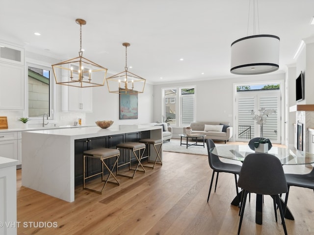 dining area featuring ornamental molding, a notable chandelier, sink, and light wood-type flooring