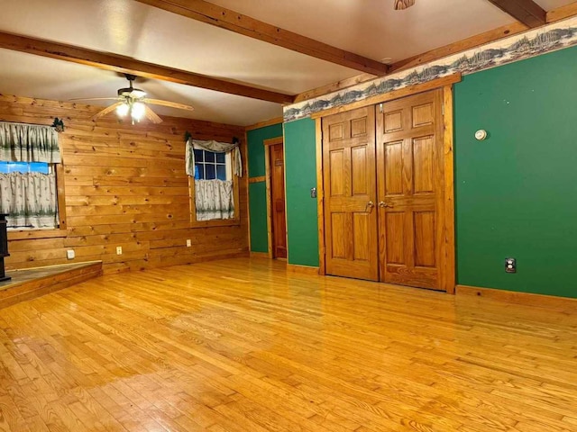 unfurnished bedroom featuring wooden walls, light wood-type flooring, and beam ceiling