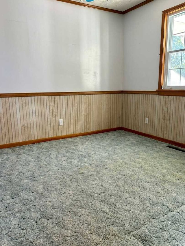 spare room with carpet, wood walls, and crown molding