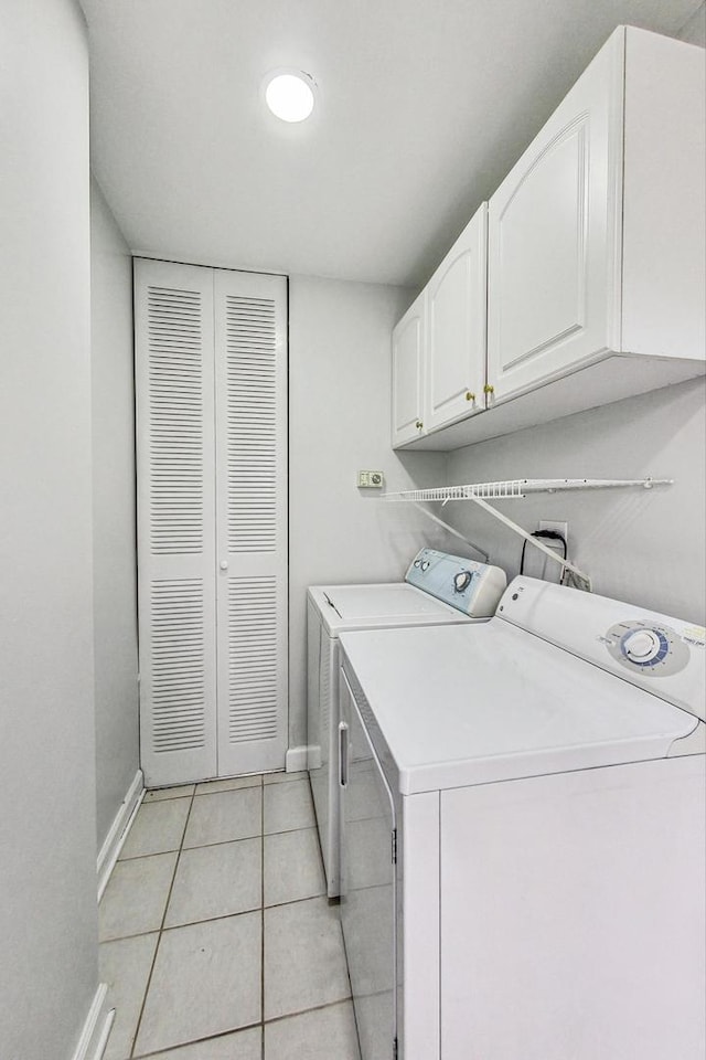 clothes washing area with light tile patterned floors, washing machine and clothes dryer, and cabinets