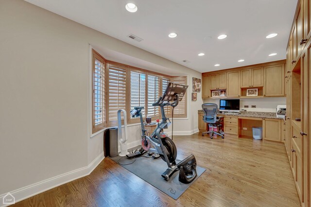 exercise area with built in desk and light hardwood / wood-style flooring