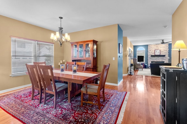 dining space with a stone fireplace, light hardwood / wood-style flooring, and ceiling fan with notable chandelier