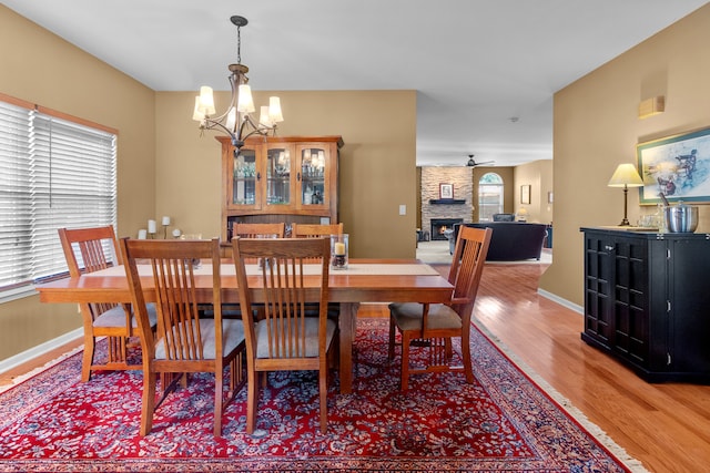 dining room featuring hardwood / wood-style flooring, a fireplace, and ceiling fan with notable chandelier