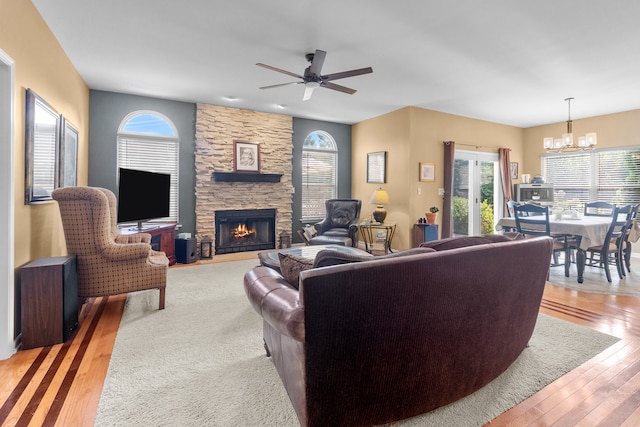 living room with ceiling fan with notable chandelier, a fireplace, and light wood-type flooring