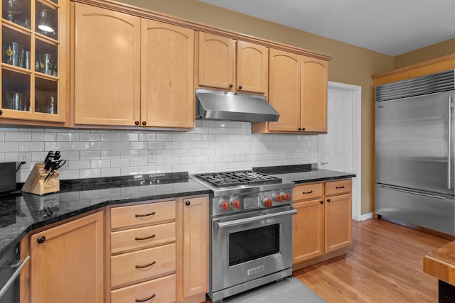 kitchen featuring high quality appliances, dark stone countertops, light brown cabinets, and light hardwood / wood-style floors