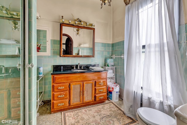 bathroom featuring toilet, tile patterned flooring, a shower with door, vanity, and tile walls