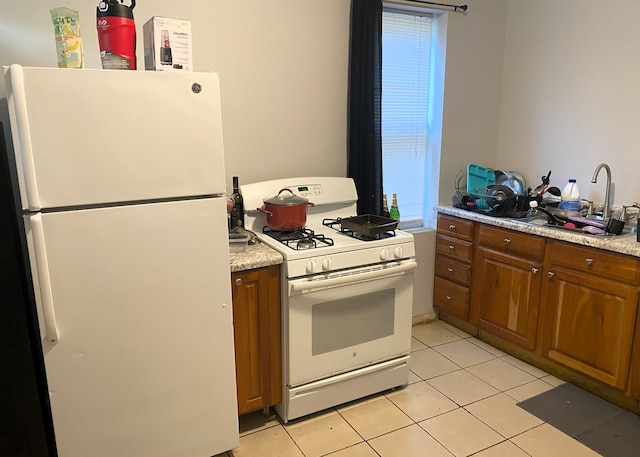 kitchen featuring white appliances, light stone countertops, light tile patterned floors, and sink