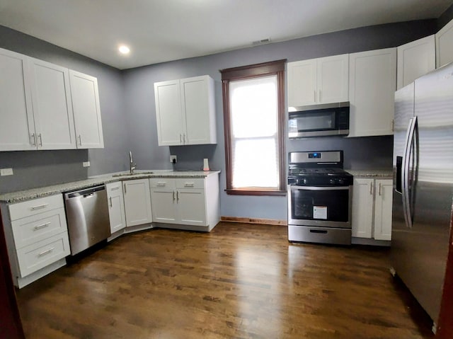 kitchen with white cabinets, light stone counters, dark wood-type flooring, and appliances with stainless steel finishes