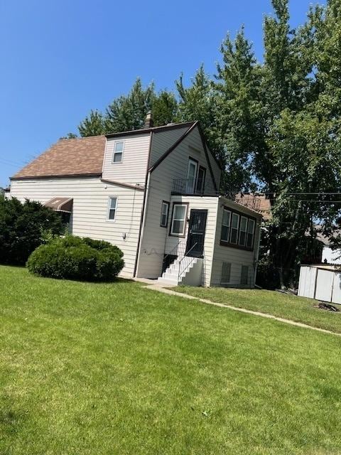 back of property featuring entry steps, a lawn, and a chimney