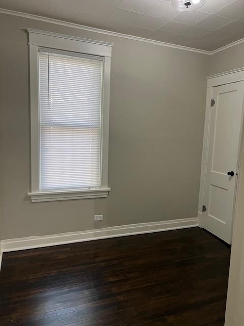 spare room with baseboards, ornamental molding, and dark wood finished floors