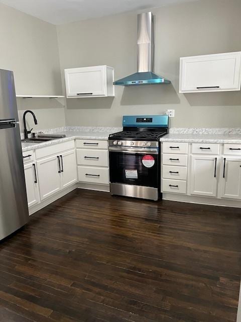 kitchen featuring dark wood-style flooring, appliances with stainless steel finishes, white cabinets, a sink, and wall chimney range hood