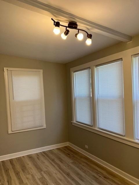 empty room featuring beamed ceiling, wood finished floors, and baseboards