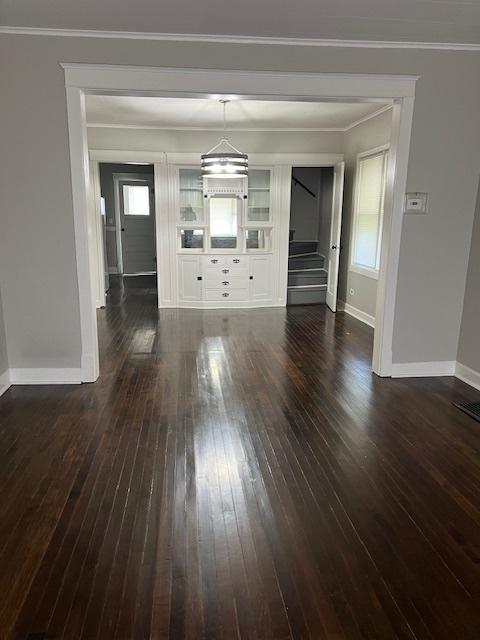 interior space featuring baseboards, ornamental molding, dark wood-style flooring, stairs, and a healthy amount of sunlight