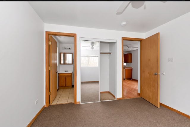 unfurnished bedroom featuring a closet, light colored carpet, ensuite bath, and ceiling fan