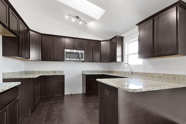 kitchen with dark brown cabinetry, stainless steel microwave, a peninsula, a sink, and lofted ceiling with skylight