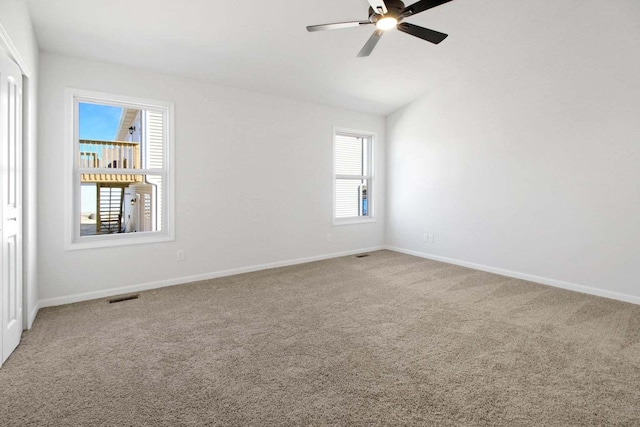 carpeted empty room with ceiling fan, visible vents, vaulted ceiling, and baseboards