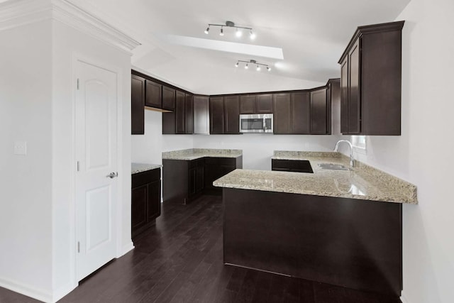 kitchen with lofted ceiling, stainless steel microwave, dark wood-type flooring, a sink, and dark brown cabinetry