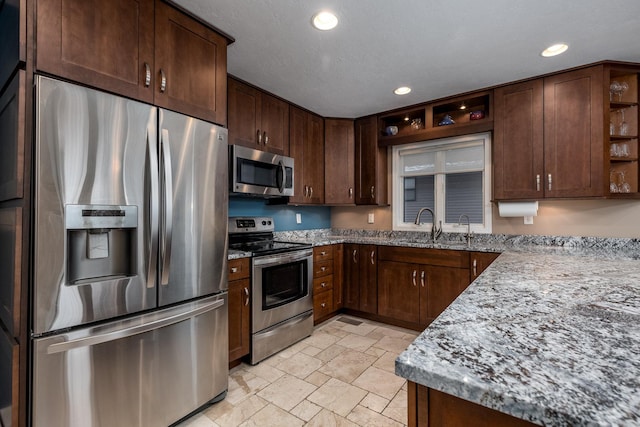 kitchen with open shelves, appliances with stainless steel finishes, stone finish flooring, a sink, and light stone countertops