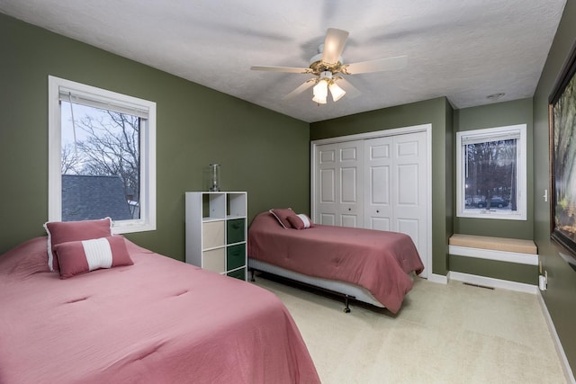 bedroom with a closet, light colored carpet, ceiling fan, a textured ceiling, and baseboards