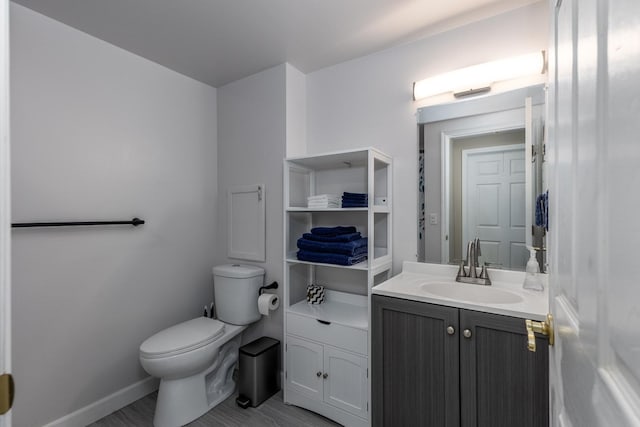 half bathroom with baseboards, vanity, toilet, and wood finished floors