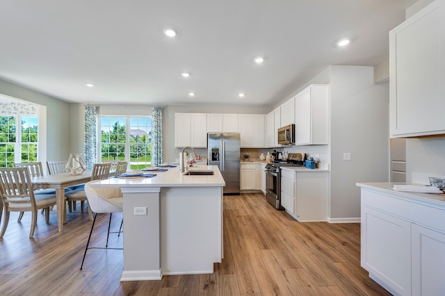 kitchen with a kitchen island with sink, white cabinetry, sink, appliances with stainless steel finishes, and light hardwood / wood-style floors