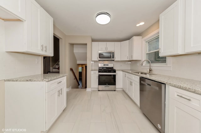 kitchen with appliances with stainless steel finishes, light stone countertops, tasteful backsplash, and sink