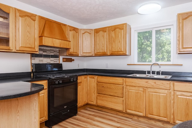 kitchen featuring a textured ceiling, light hardwood / wood-style flooring, custom range hood, black range with gas cooktop, and sink