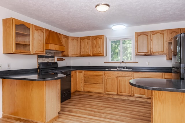 kitchen featuring light hardwood / wood-style flooring, stainless steel fridge, black gas stove, custom range hood, and sink