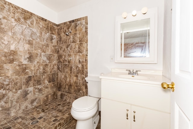 bathroom with toilet, tiled shower, and vanity