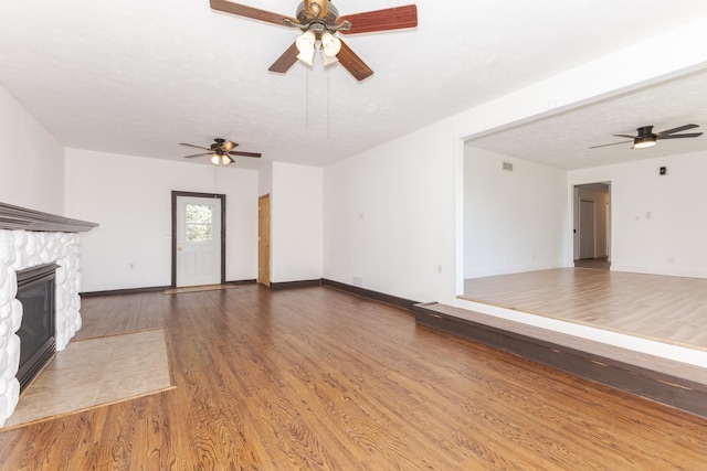 unfurnished living room with hardwood / wood-style floors, a textured ceiling, ceiling fan, and a stone fireplace