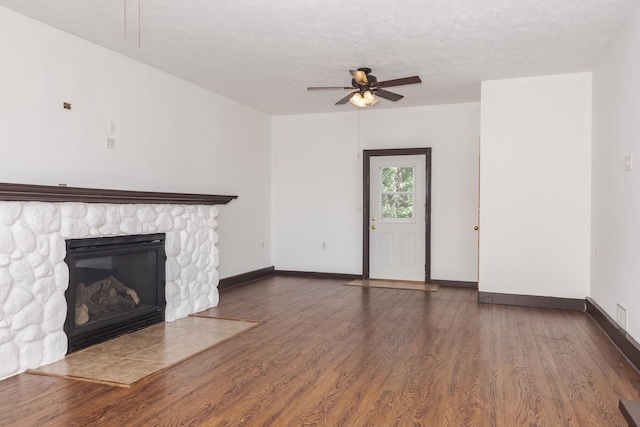 unfurnished living room with dark wood-type flooring, ceiling fan, a textured ceiling, and a stone fireplace