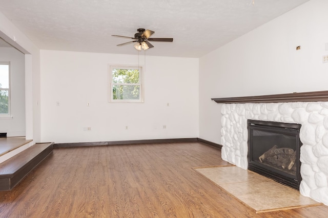 unfurnished living room featuring ceiling fan, wood-type flooring, and a stone fireplace