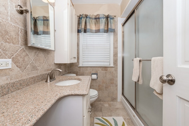 bathroom with a shower with door, vanity, tile walls, toilet, and decorative backsplash