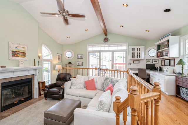 living room featuring light hardwood / wood-style flooring, ceiling fan, a tile fireplace, and vaulted ceiling with beams