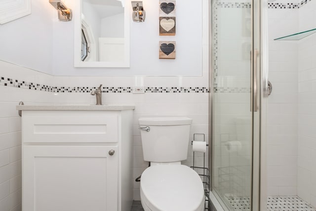 bathroom with vanity, toilet, a shower with shower door, and tile walls