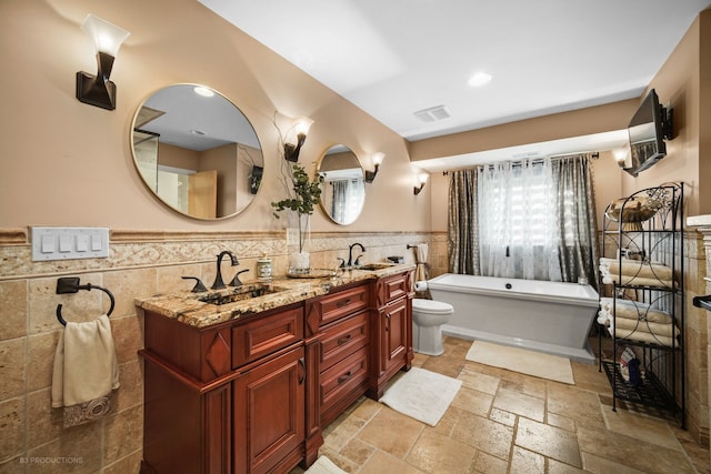 bathroom with tile walls, toilet, vanity, and a washtub