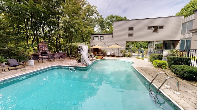 view of swimming pool featuring a water slide, a patio, and a fireplace