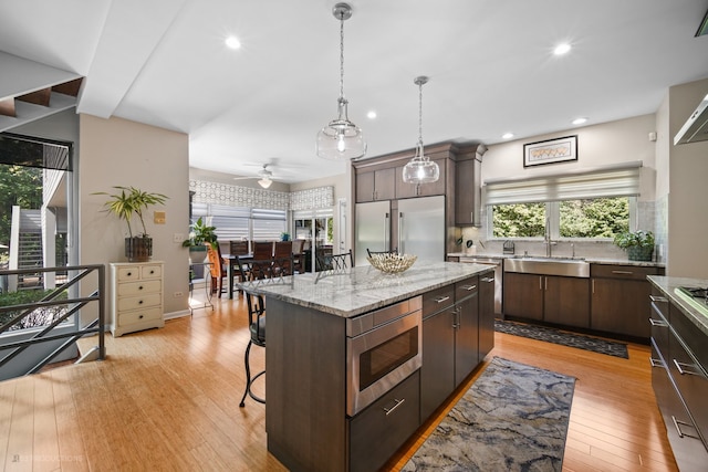 kitchen with a kitchen island, built in appliances, ceiling fan, and light hardwood / wood-style floors