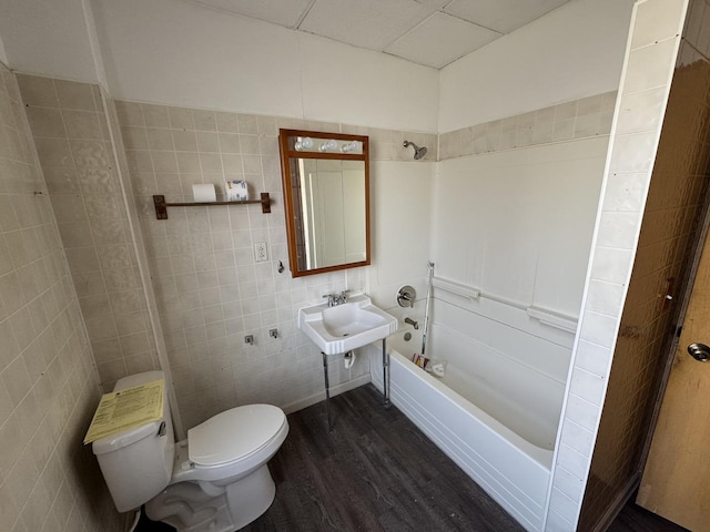 full bath featuring toilet, bathtub / shower combination, wood finished floors, tile walls, and a sink