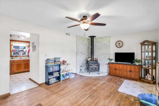 living room with light hardwood / wood-style flooring, a wood stove, and ceiling fan