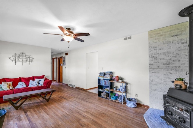 living room with hardwood / wood-style flooring, ceiling fan, and a wood stove